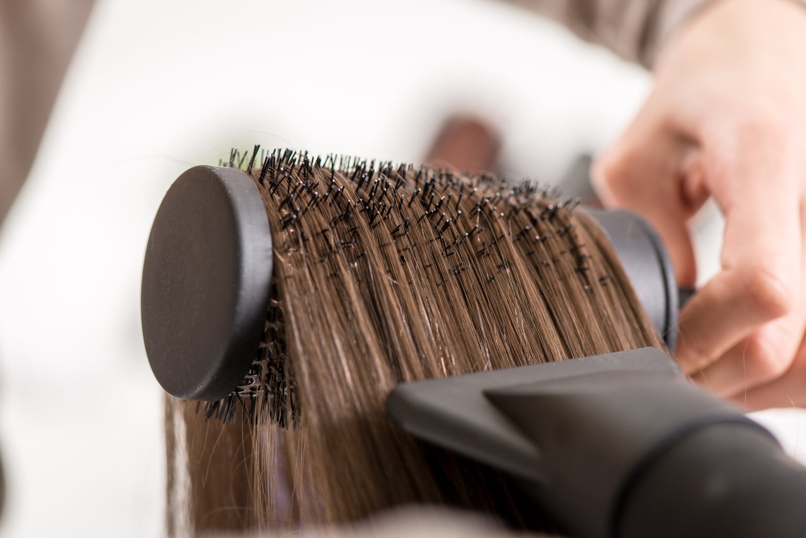 Close-up of a drying brown hair with hair dryer and round brush.